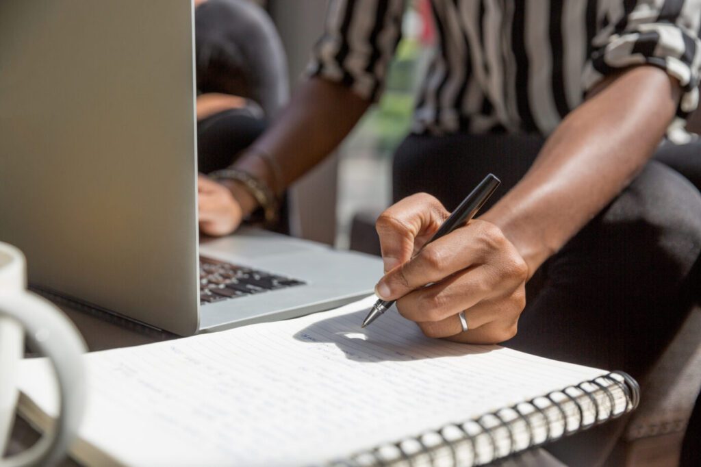 Man working on a laptop and writing in a notebook